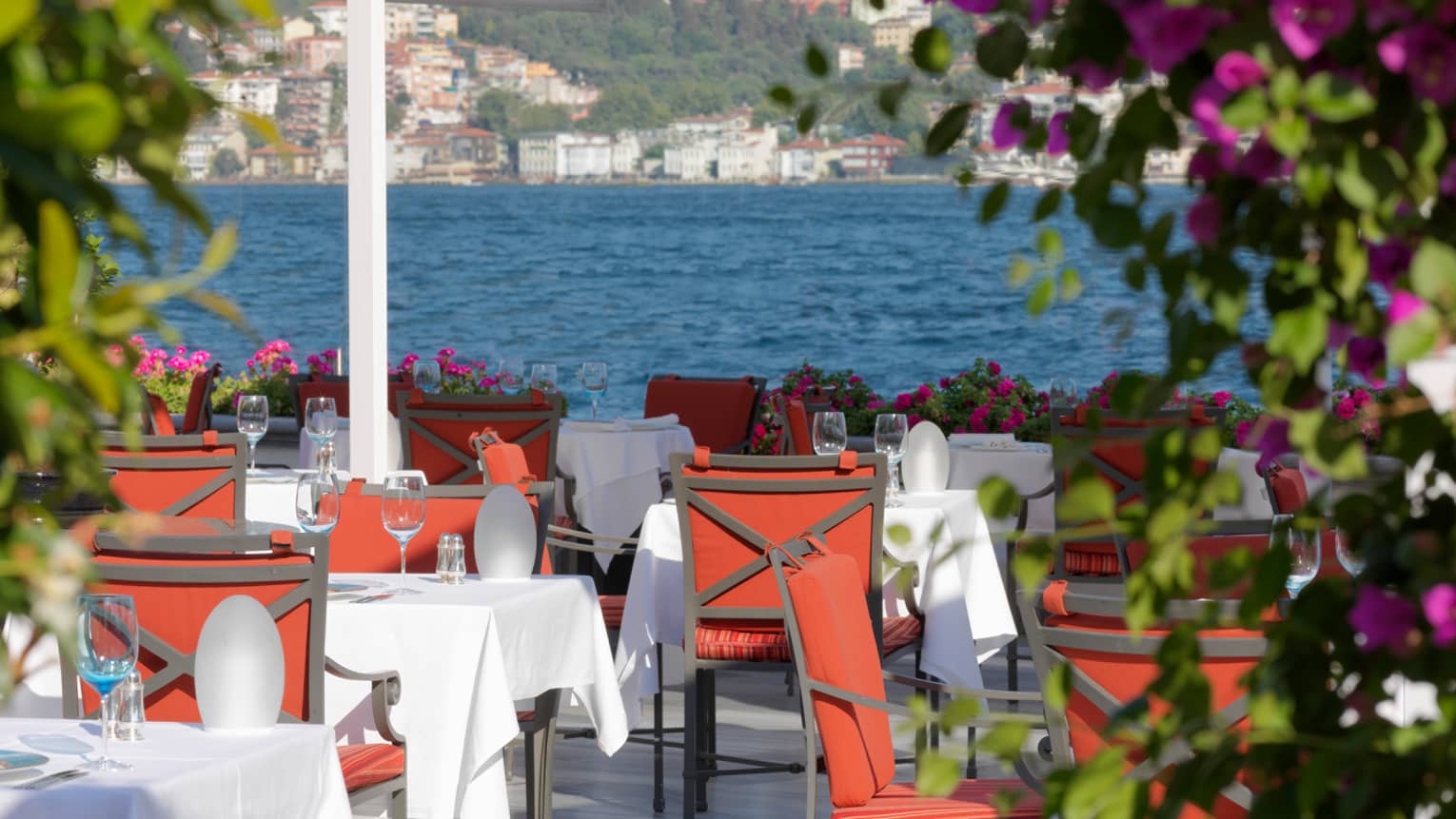 Red dining chairs, tables with white cloths on sunny Aqua restaurant patio
