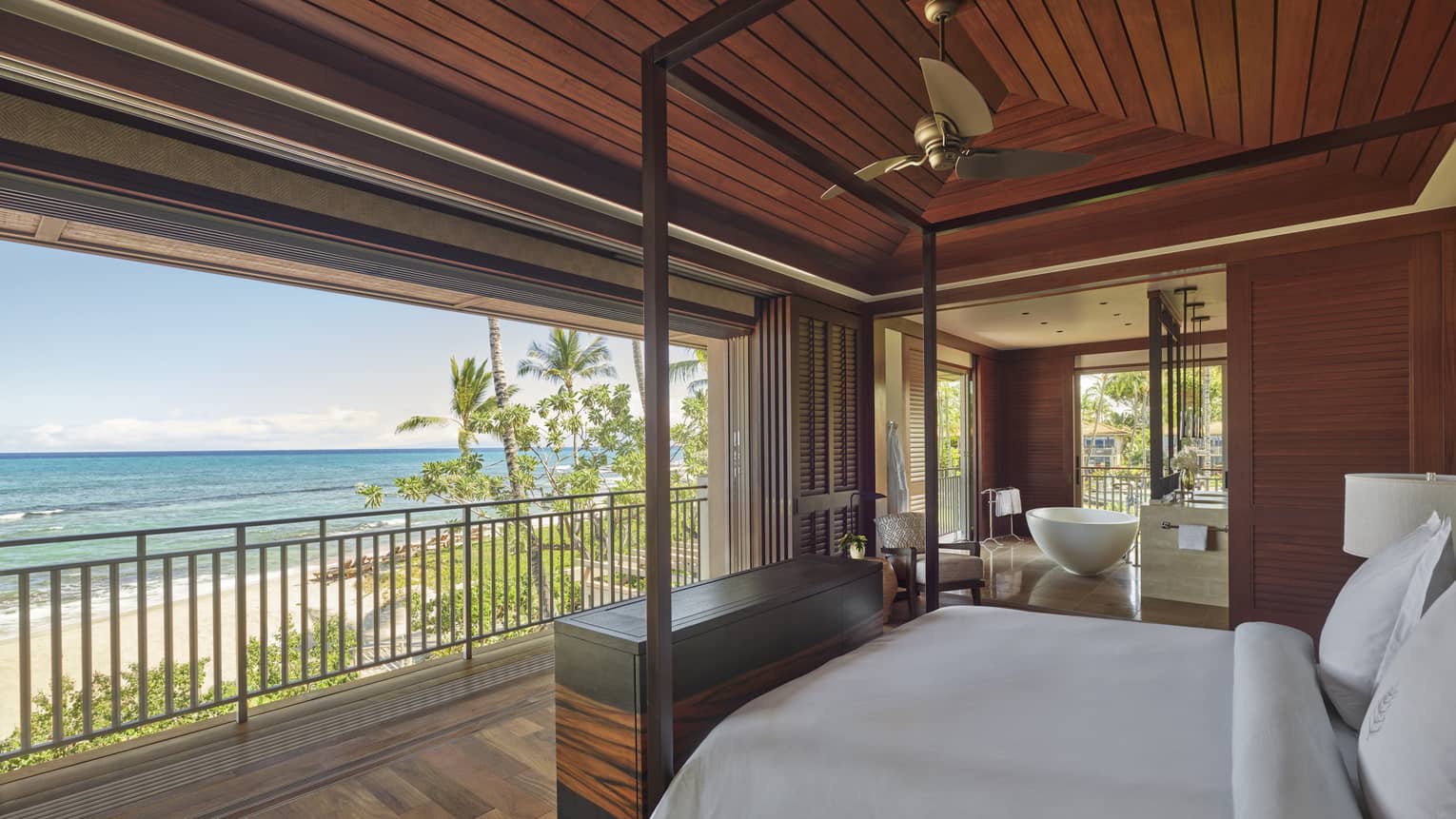 Bedroom with white king bed facing open wall, which looks out to tropical beach