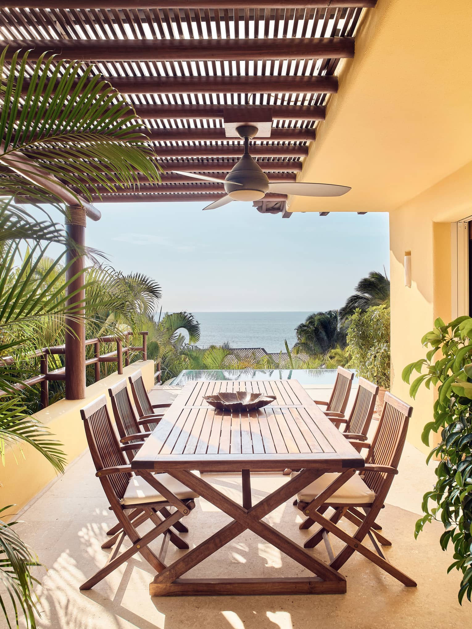Wood patio table, chairs under pergola and ceiling fan, ocean views