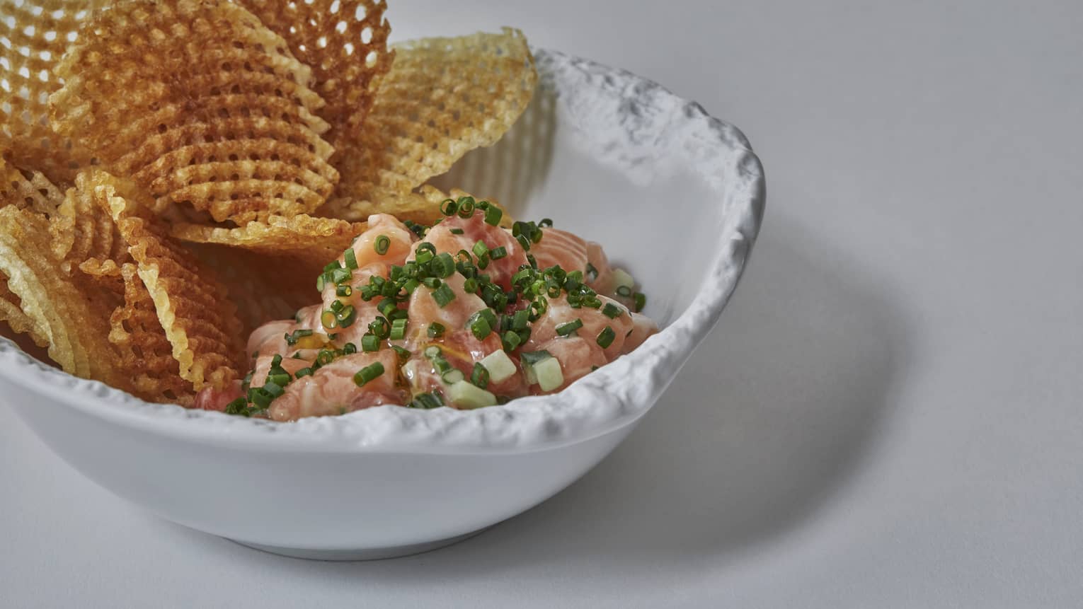 A waffle fry and salmon dish in a white porcelain bowl
