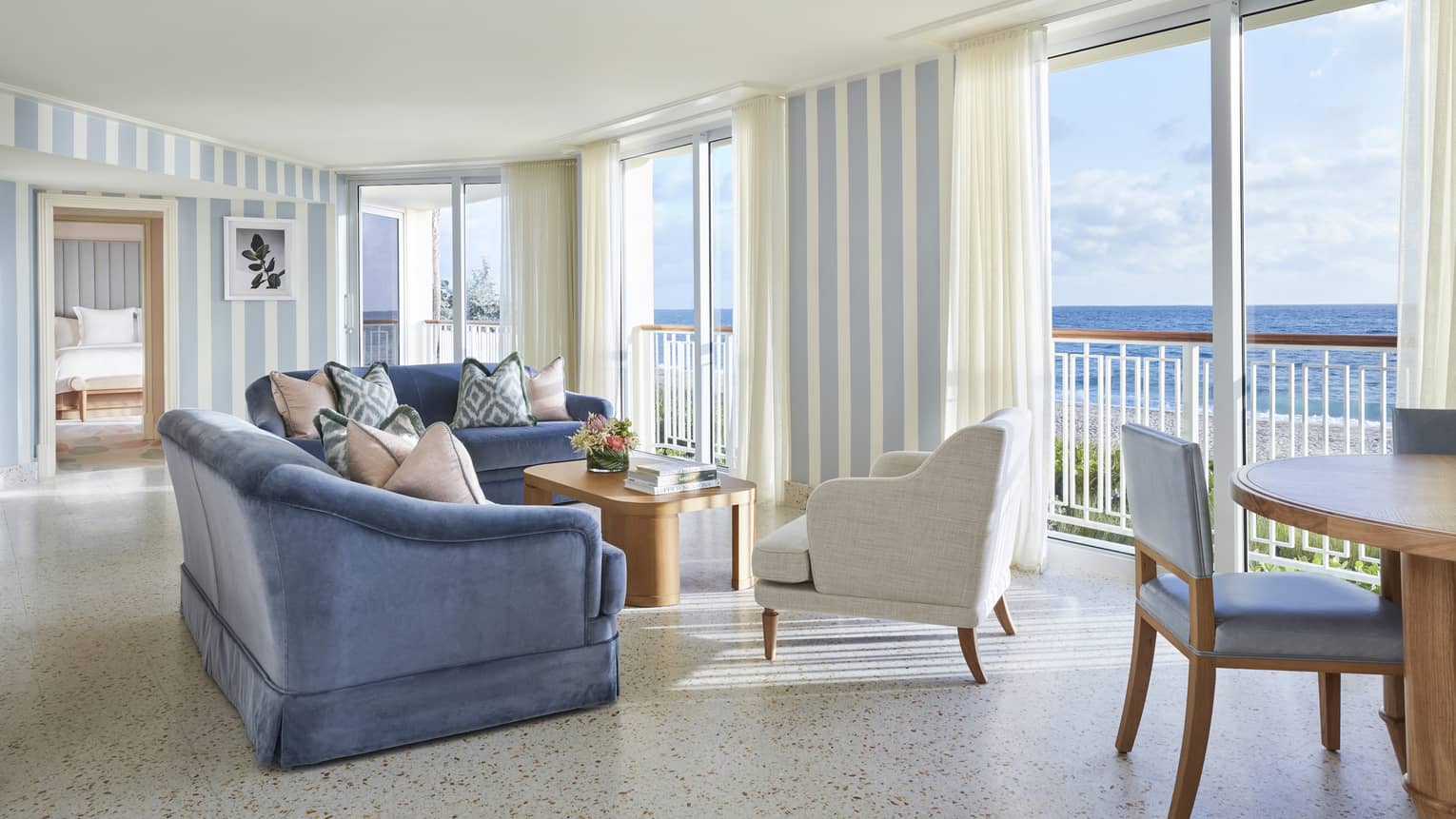 Living area in a suite, with blue sofas, a white armchair and floor-to-ceiling views of the ocean
