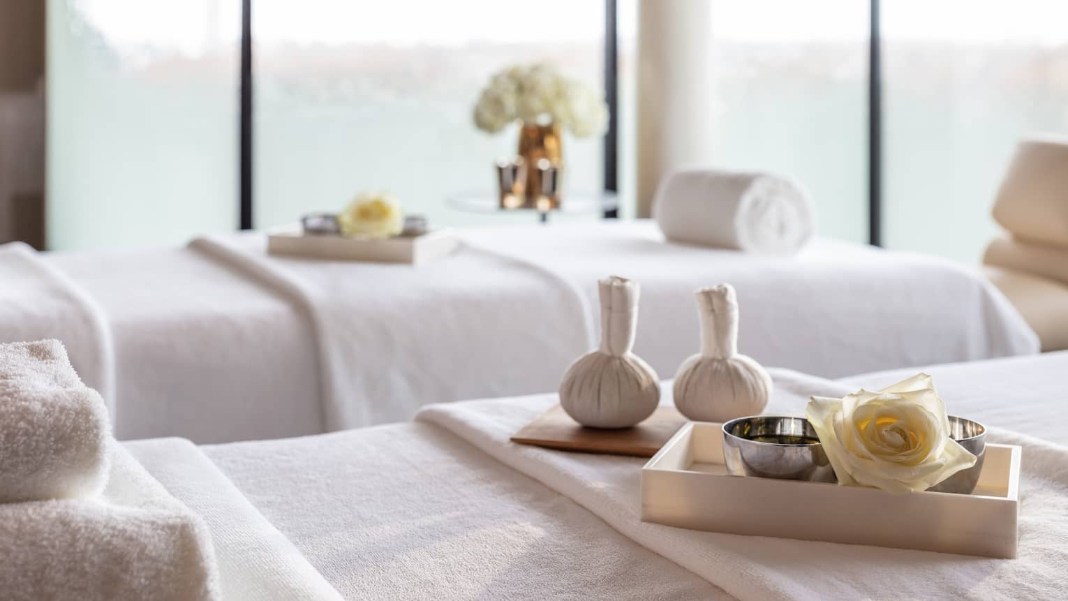 Spa couples treatment room with two white beds, one with tray, bowls and rose