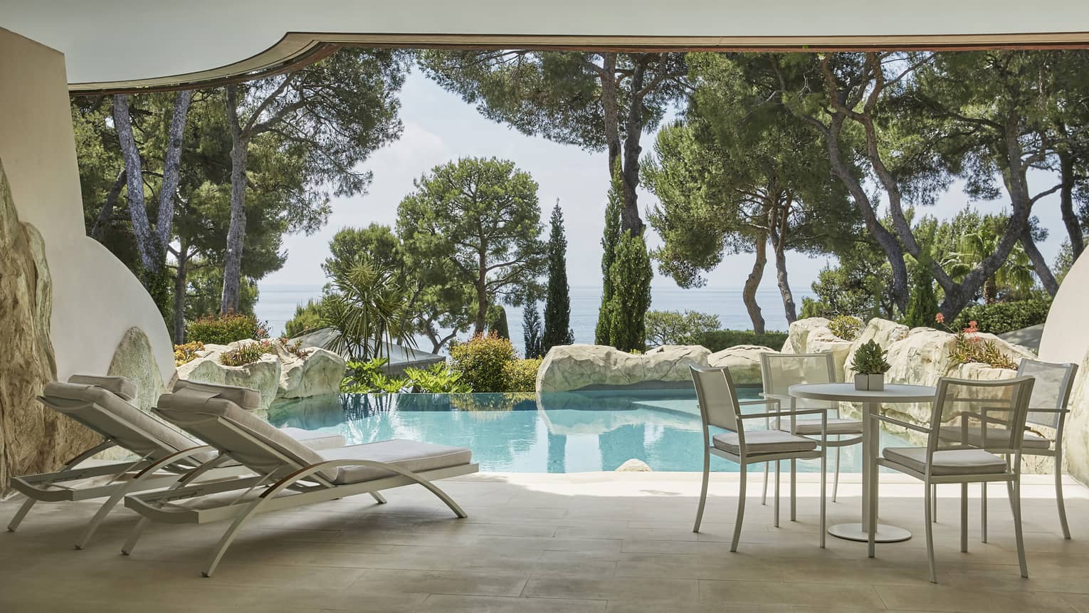 Private stone pool and terrace with two lounge chairs, table and chairs, sea view through greenery