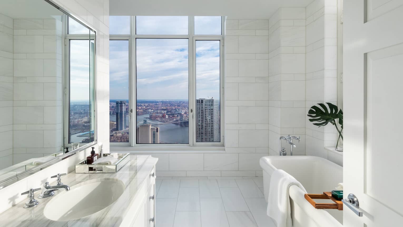 White marble bathroom, vanity, towel over tub by large picture window