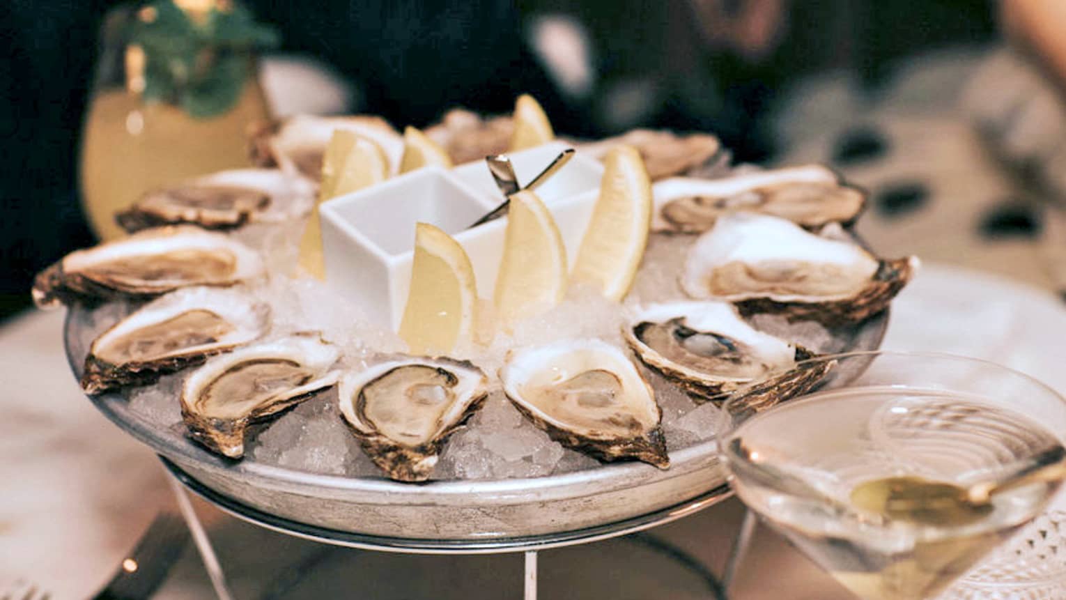 A dozen raw oysters around an ice platter with three lemon wedges in centre