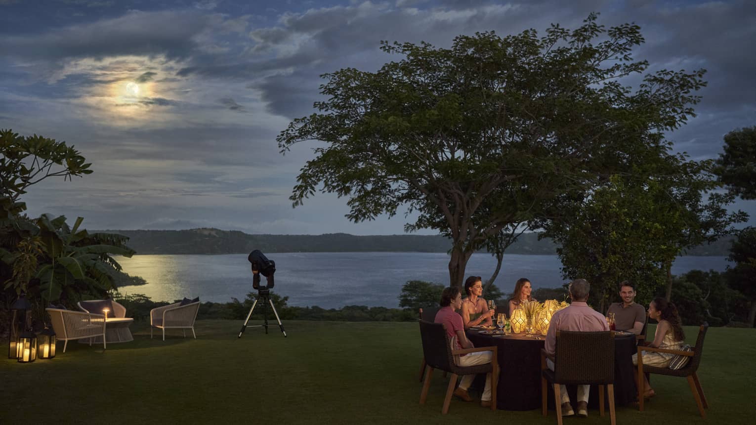 Under a golden moon, a group of diners enjoy a candlelit dinner in a clearing amid trees, a telescope positioned nearby.