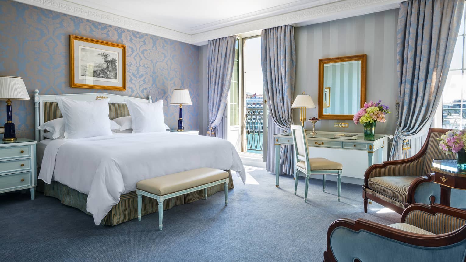 Deluxe Room bed with elegant blue-and-gold wallpaper and decor, floor-to-ceiling French doors opening to patio