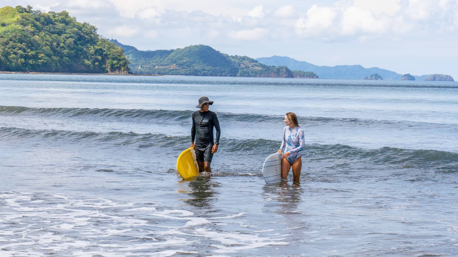 A surf instructor and student walk out of the water side by side and each holding their surfboard