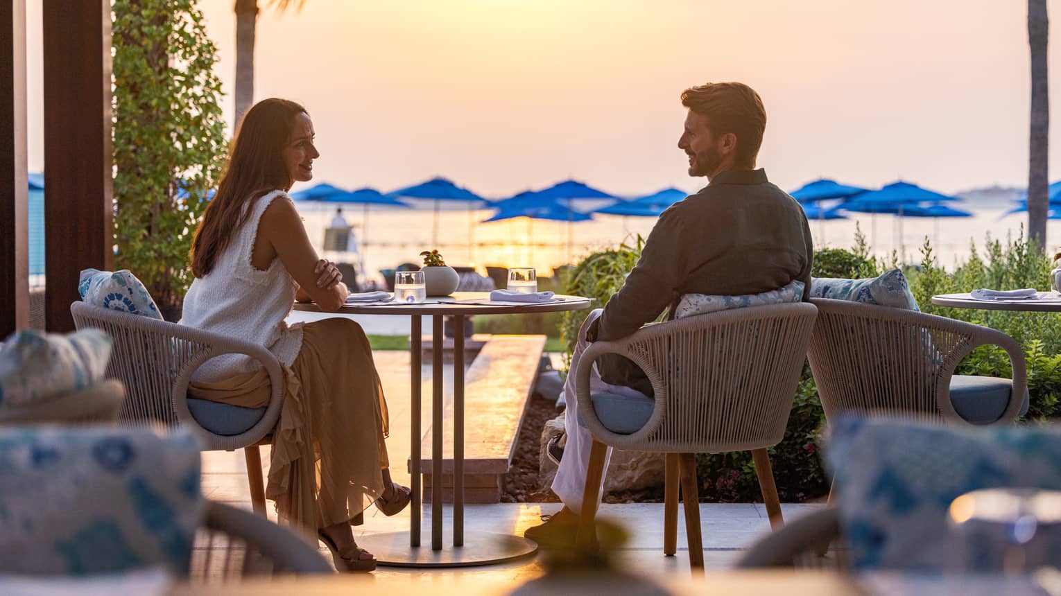 Couple sits at a table overlooking the ocean at sunset