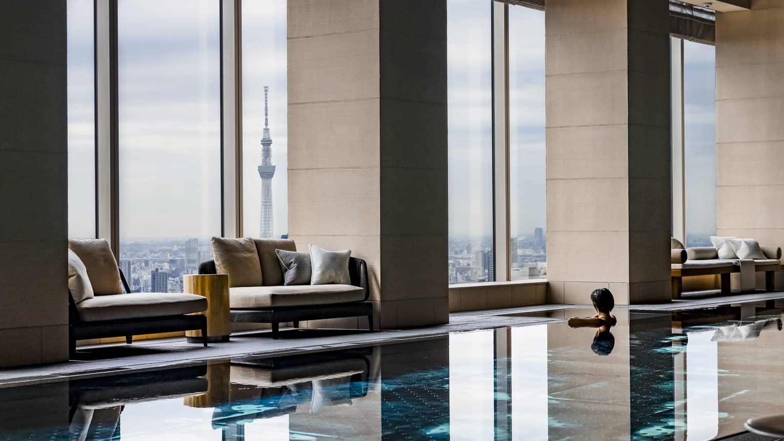 Indoor pool with sparkling cerulean water, pool chairs and floor-to-ceiling windows overlooking the city