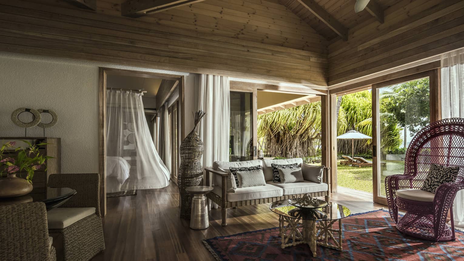 One-bedroom suite living room wicker furniture under wood beam roof, bed with white sheer canopy