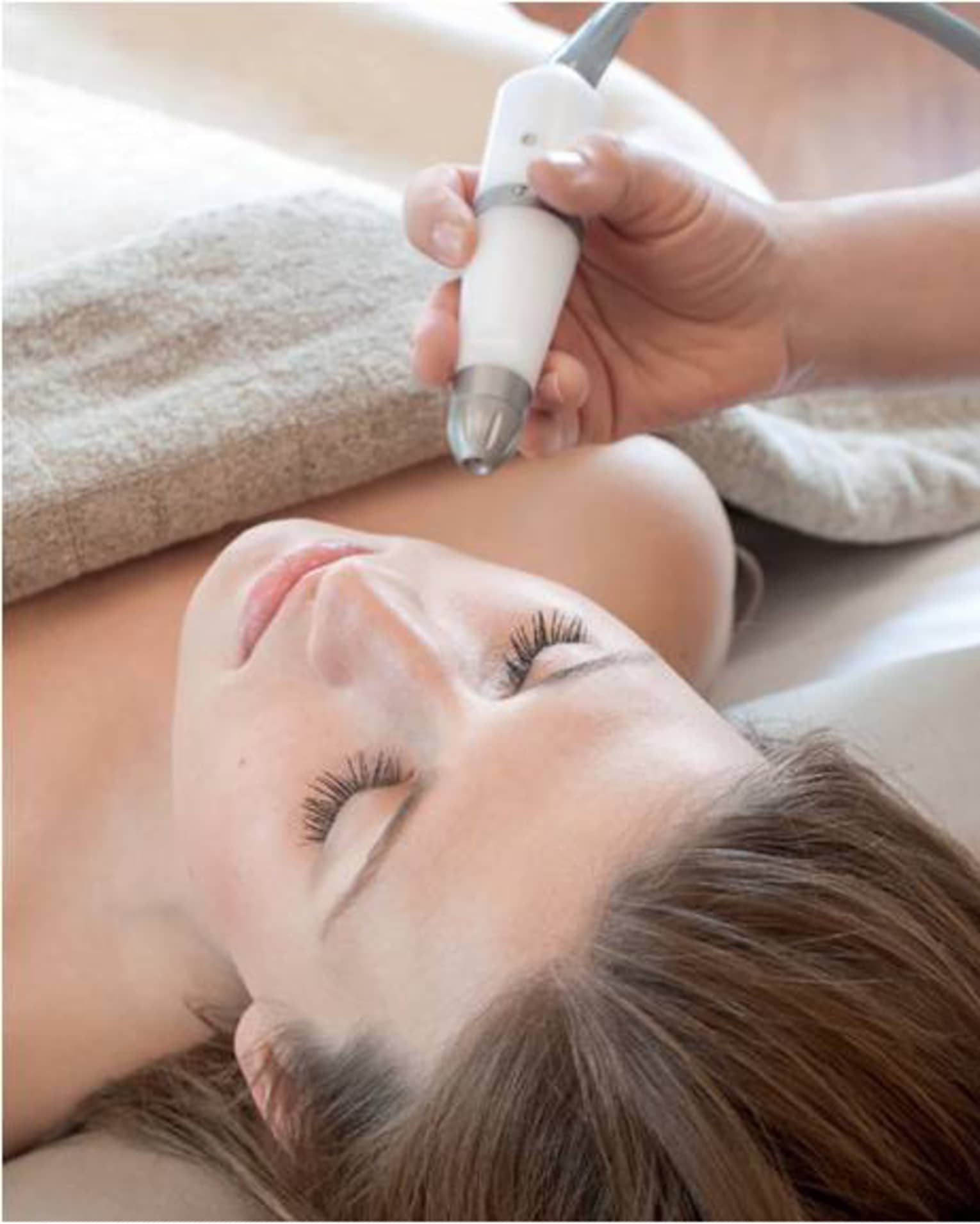 A woman in a spa getting a laser treatment on her face, the staff member is holding the device.