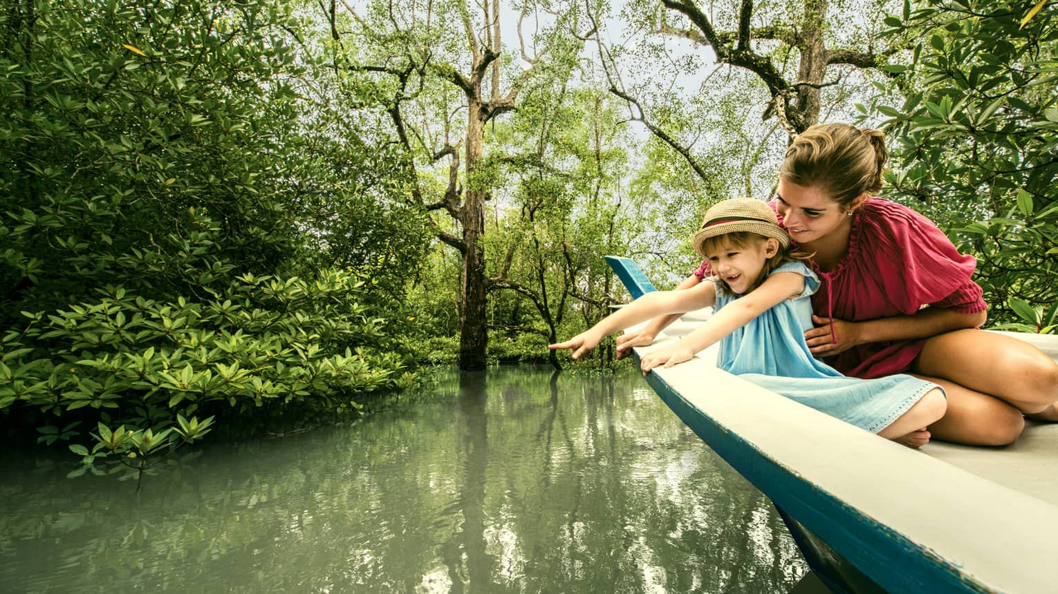 Mom, young daughter in back of wood canoe look into river