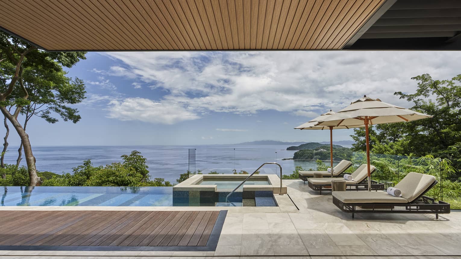 Private villa pool deck with cushioned lounge chairs, hot tub and sea view