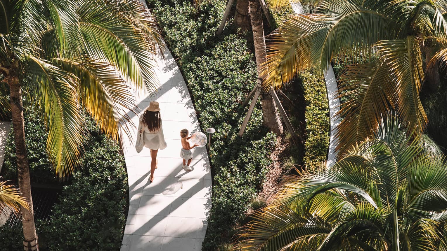 A woman and child walking along a path surrounded by plants and trees.