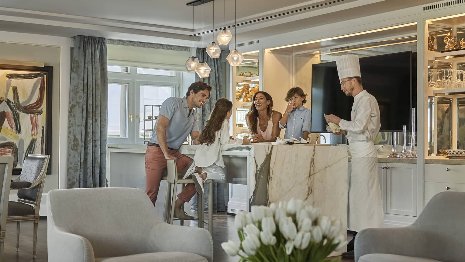 A family of four hanging around a kitchen island as a private chef prepares a meal