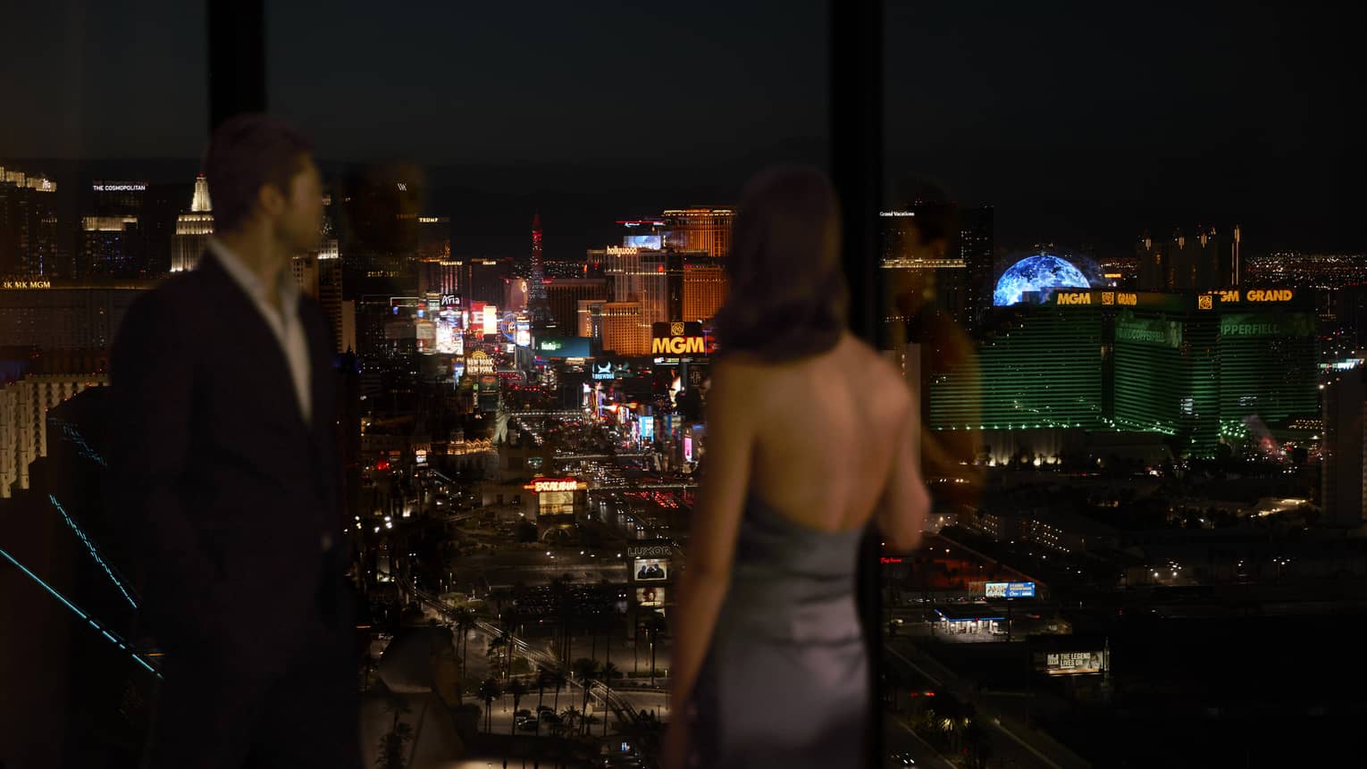 A man and woman looking out at a city covered in lights at night.