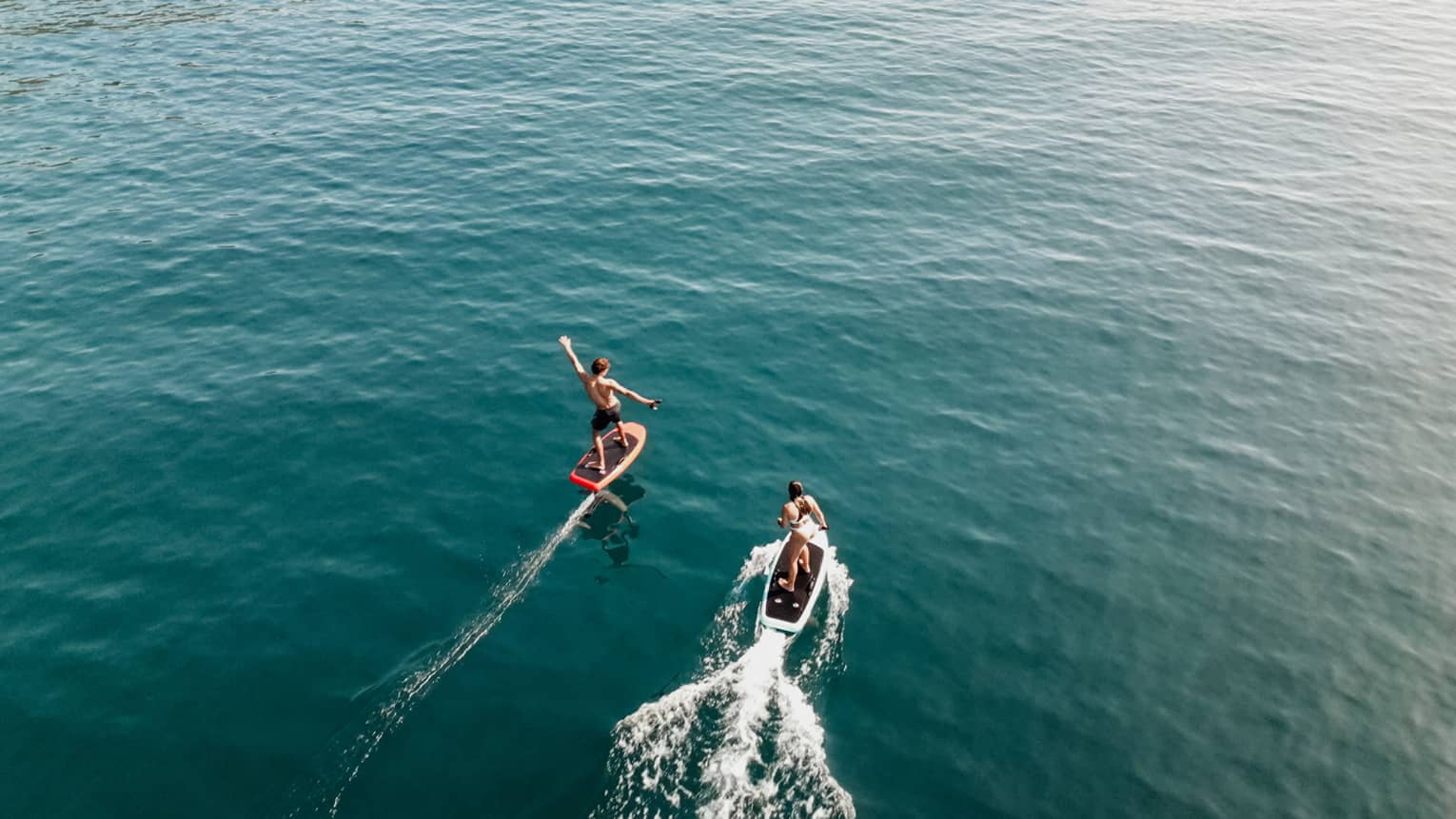 Aerial view of two people riding e0foil surfboards on blue-green water