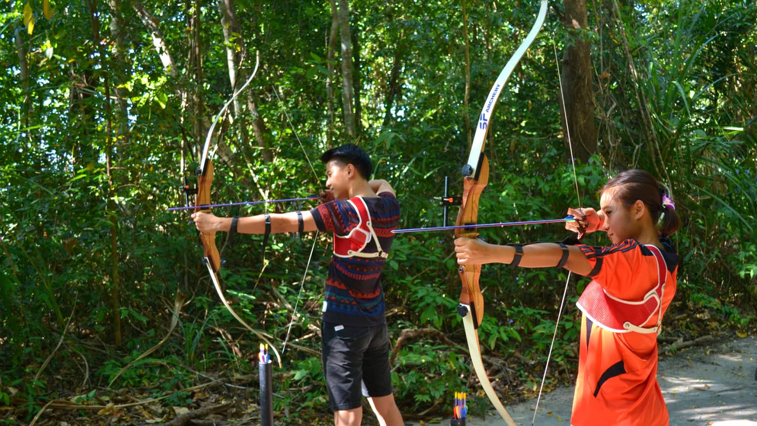 Man and woman stand with archery bow and arrows, prepare to shoot