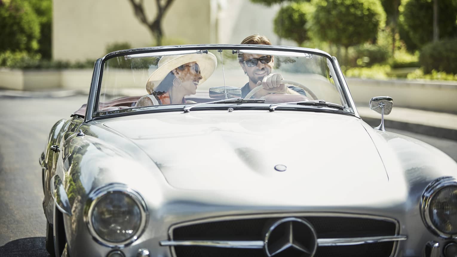 Smiling couple drive in silver luxury convertible car on sunny day