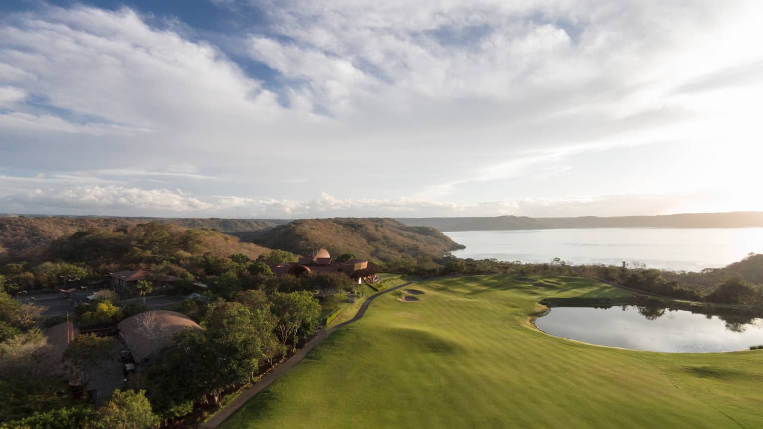 Overlooking large green golf course, forest canopy with green mountains, ocean in background