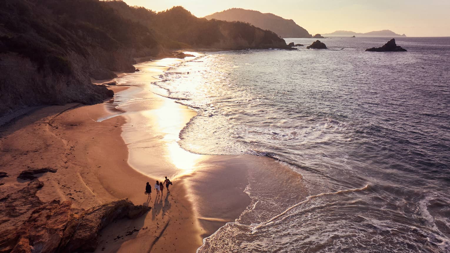 A group of people walking along a beach shore during sunrise.