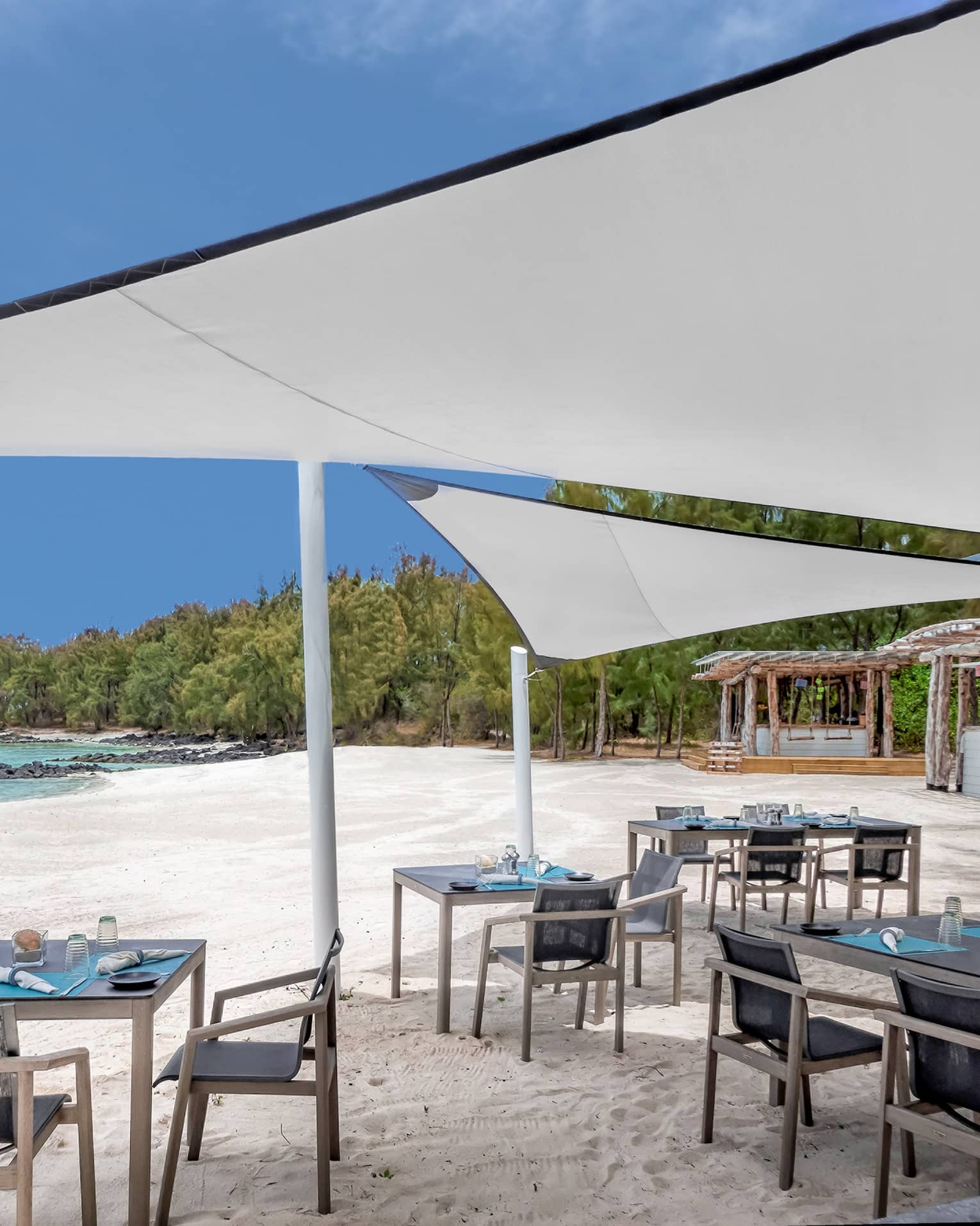 Small dining tables under white umbrella canopies on white sand beach near ocean