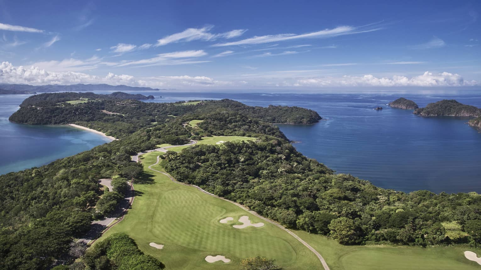Aerial view of a golf course that stretches along a verdant peninsula by the sea