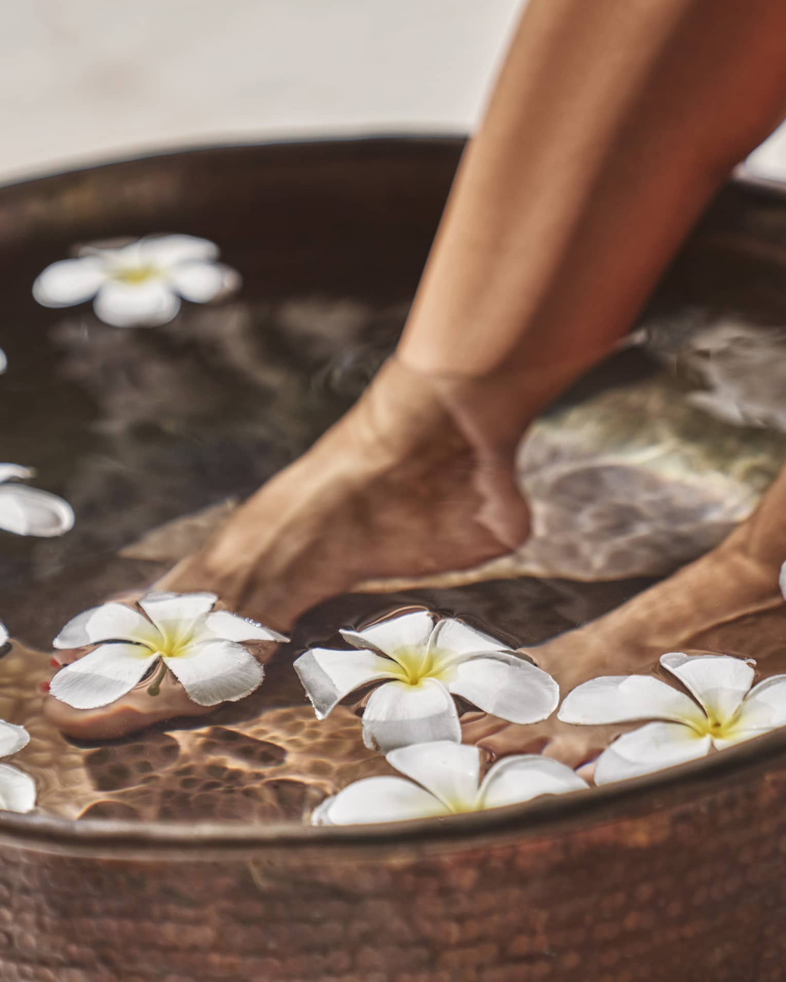 A woman's feet in a bowl of water and flowers.