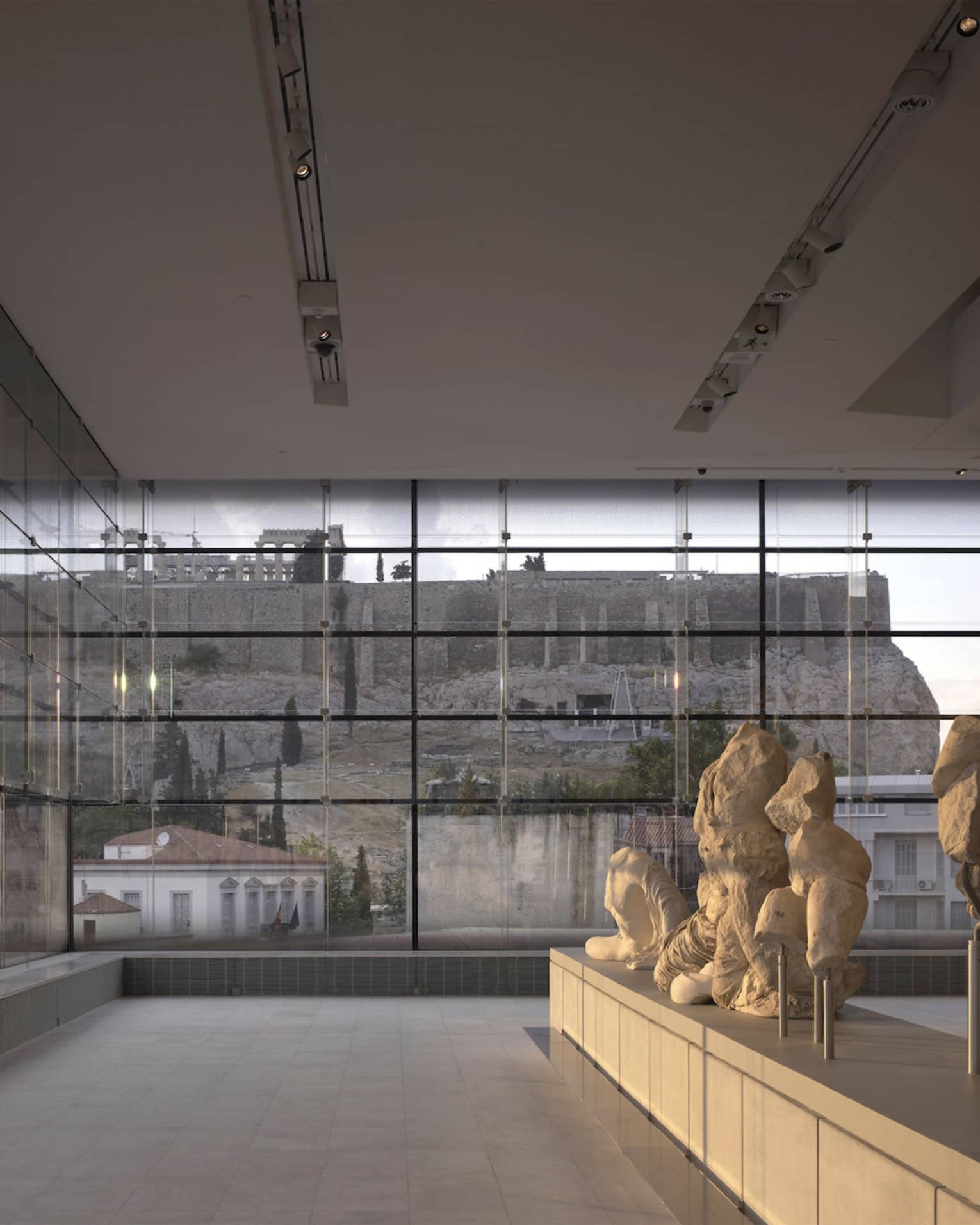 Greek sculptures on display in glass room overlooking ruins at Acropolis Museum