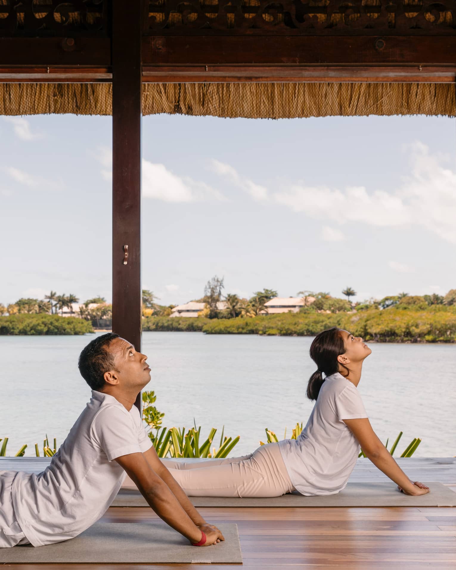 Two people practising yoga in an open to outside area.