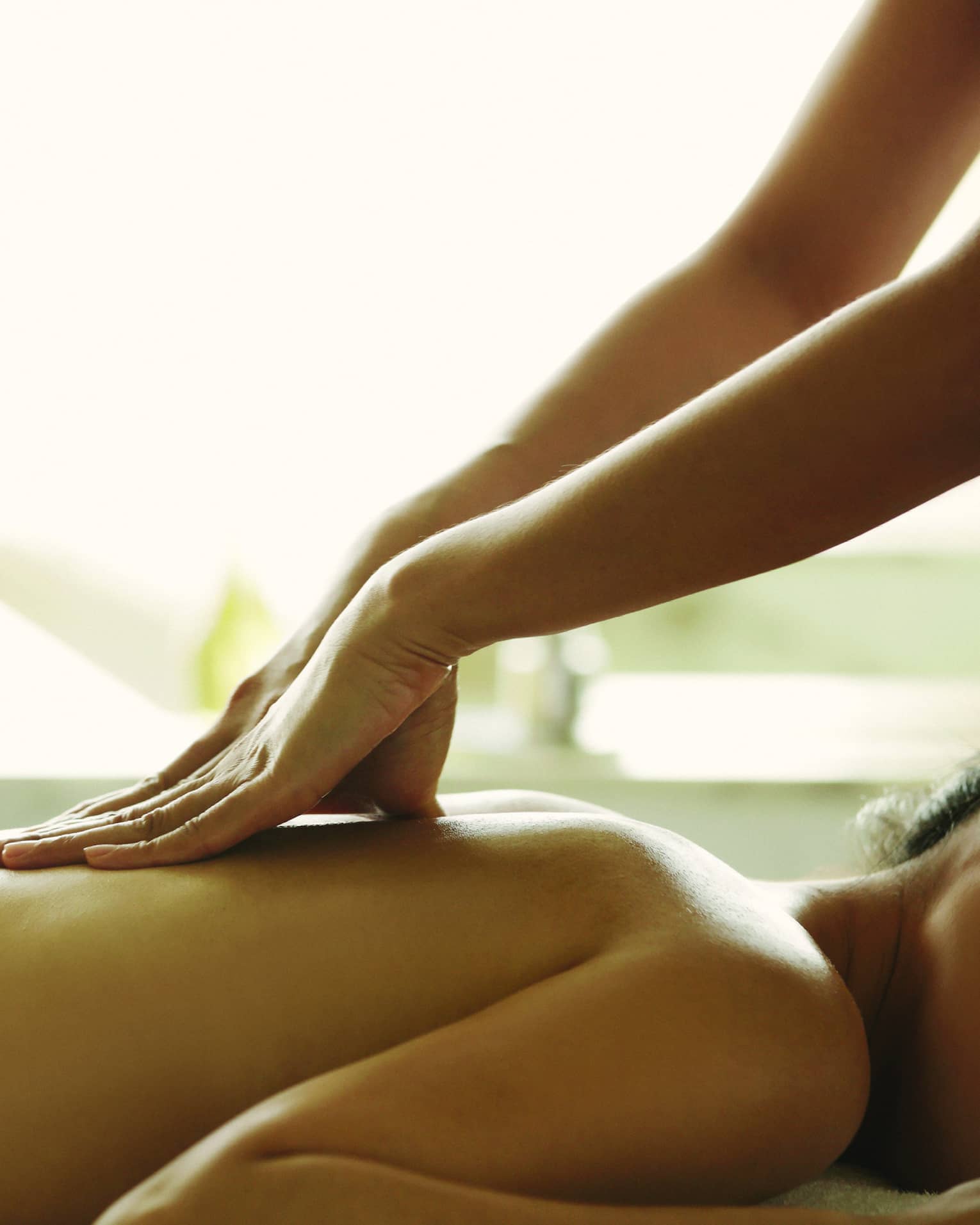 Masseuse reaches over, massages woman's bare back as she lies on spa table