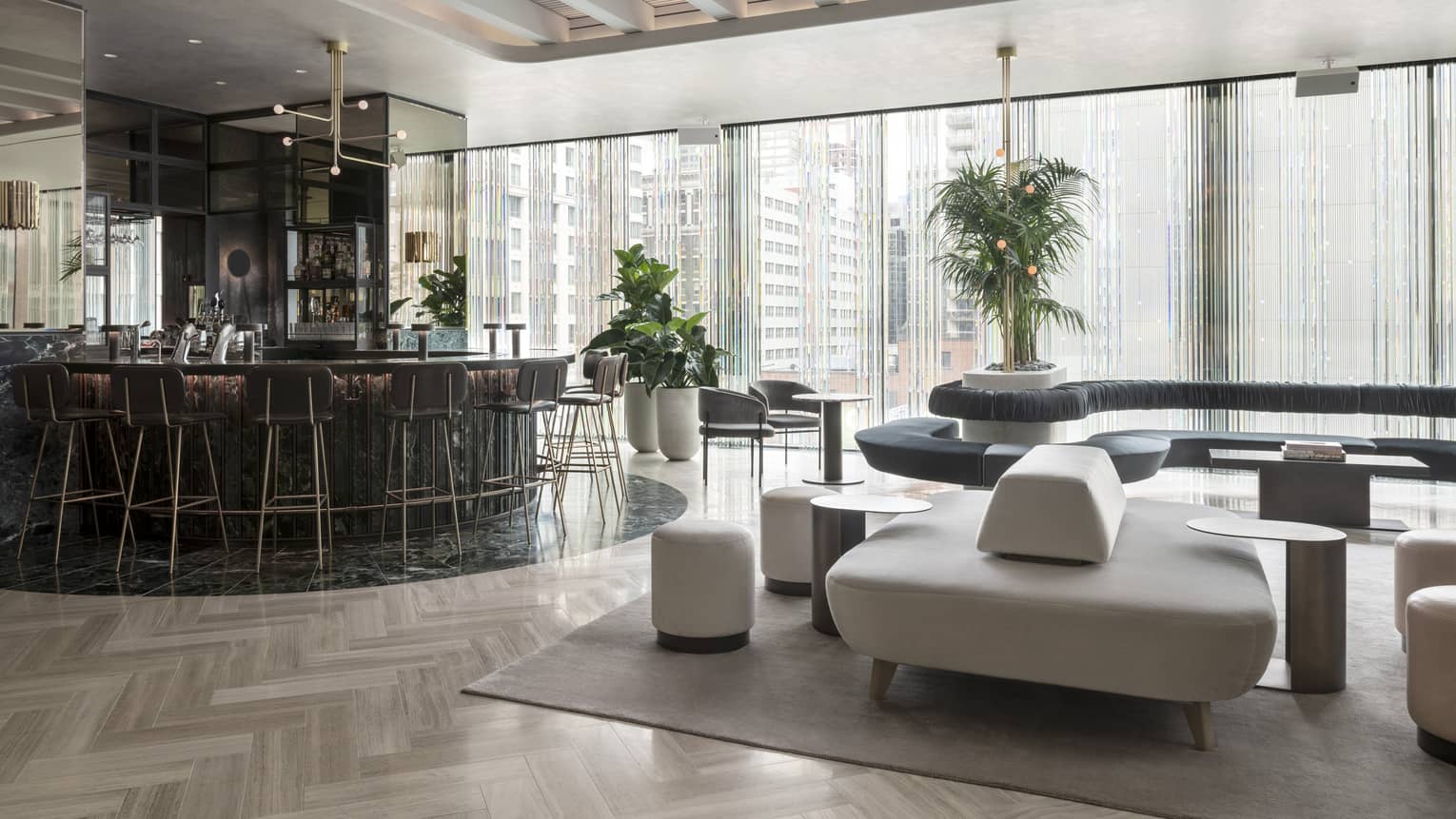 A curved black marble bar, modern grey and black furniture and a wall of windows sit beneath tall beamed ceilings at MARCUS Day Bar