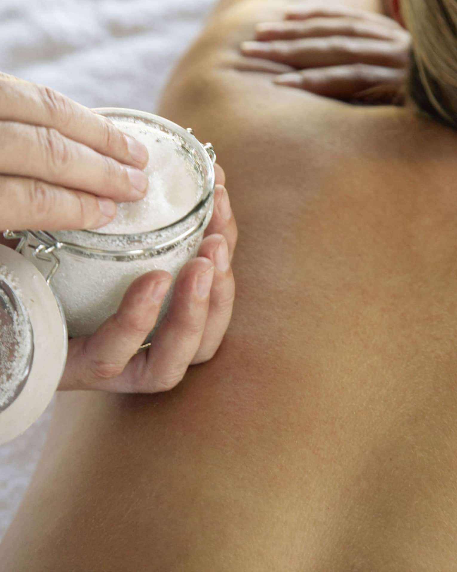 Jar of sea salt scrub above woman's bare back in spa