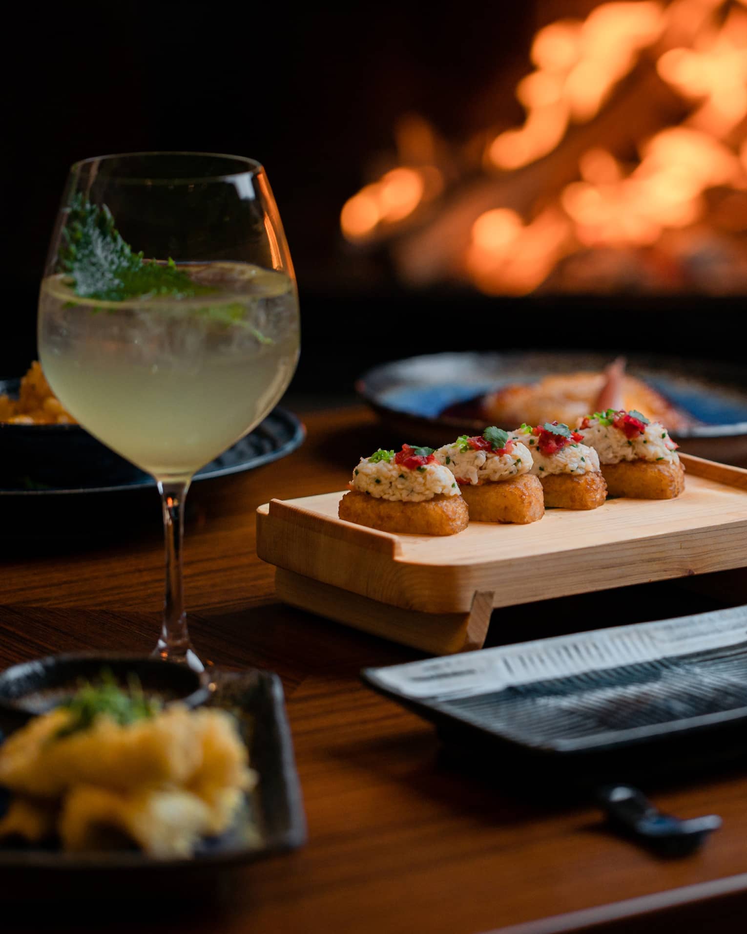 Sushi dinner setup on table with glass of white wine and sparkling fire in backdrop