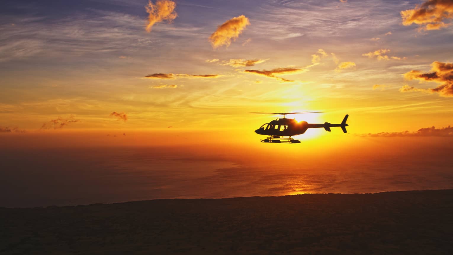 Silhouette of helicopter against orange sunset