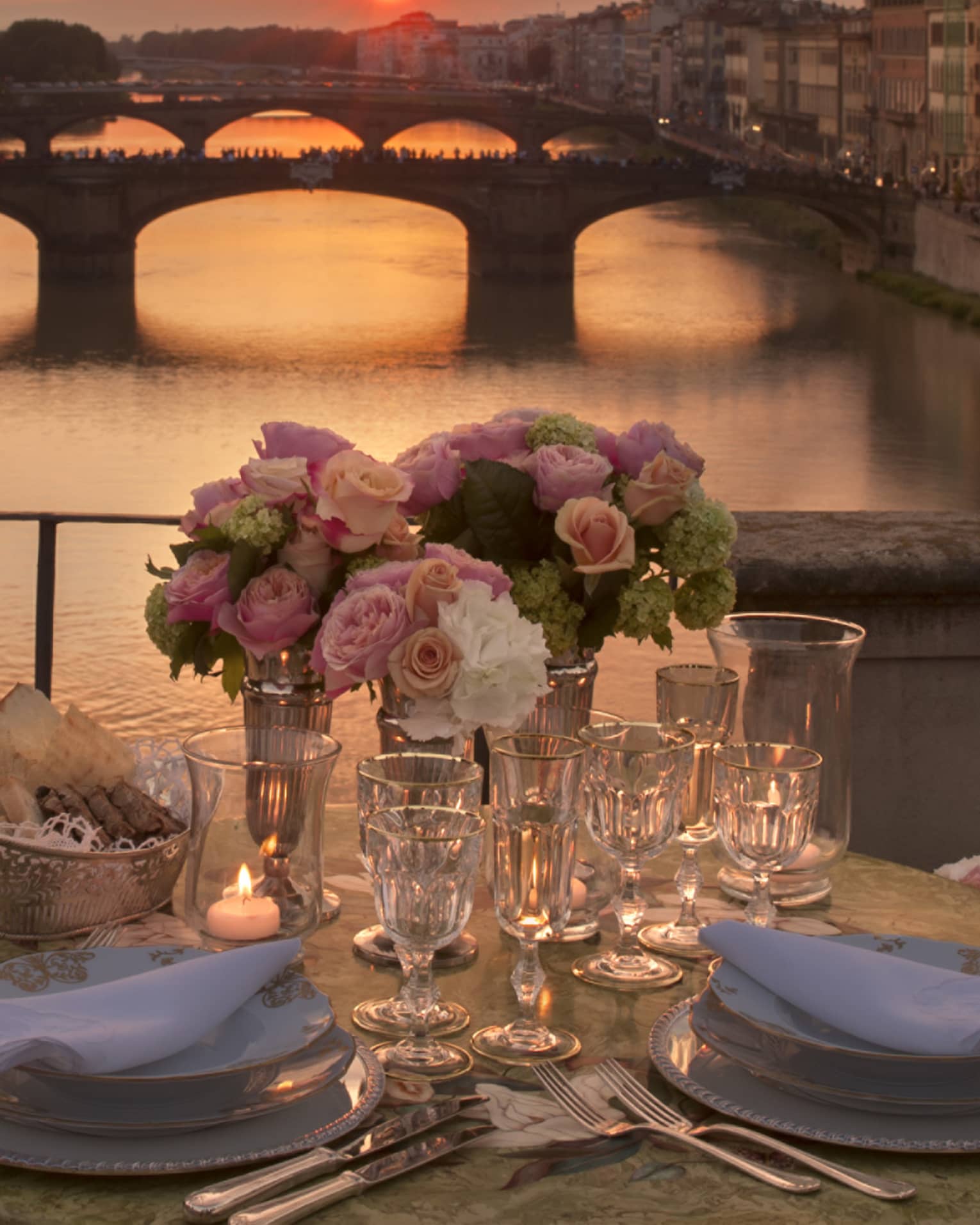 Pink roses in vases on formal dining table on bridge overlooking canal, sunset