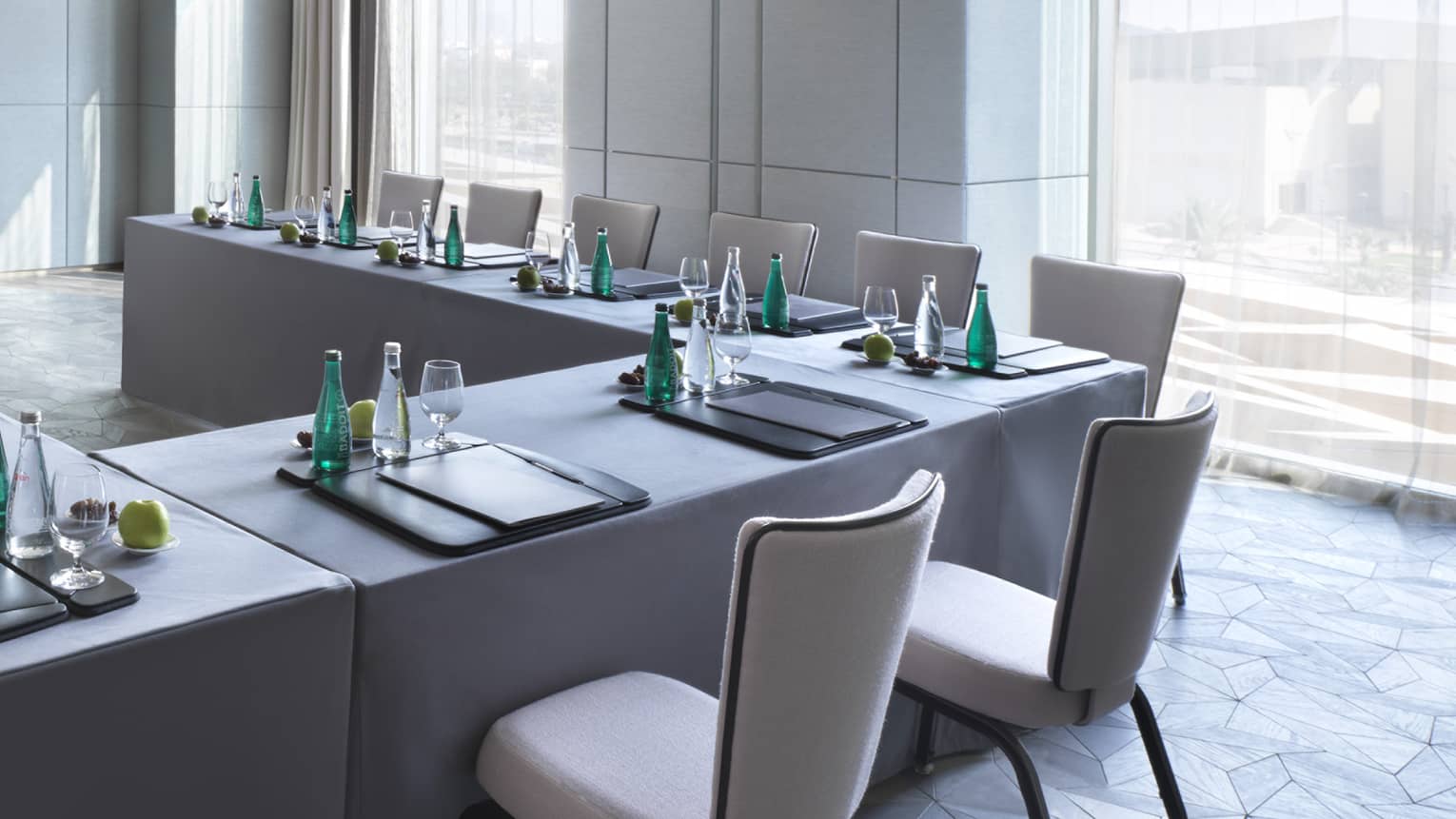 U-shaped desks with water, stationery and fruit in light-filled meeting room facing TV screen