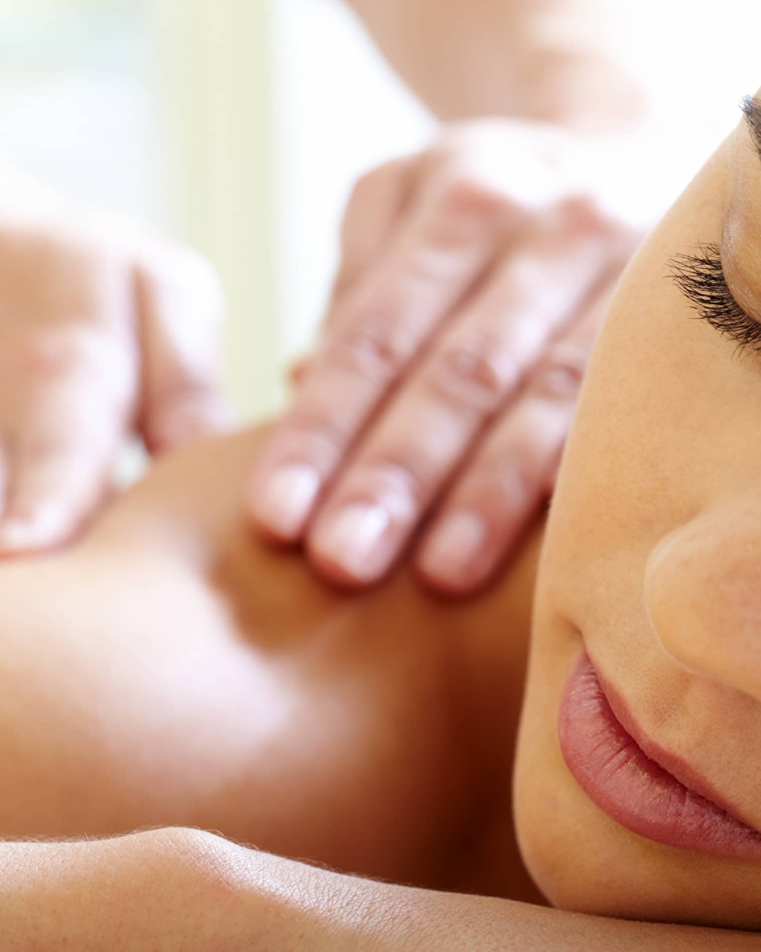 Close-up of woman's face with eyes closed, bare shoulder as she gets a Balinese massage