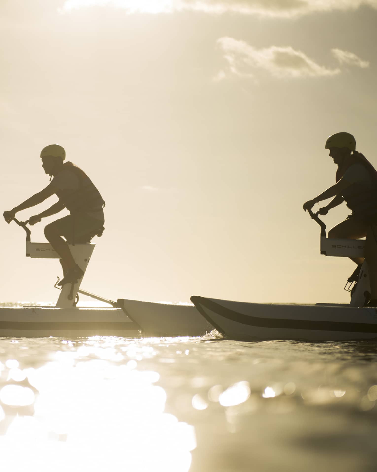 Silhouettes of two men riding aquatic bicycles on ocean at sunset