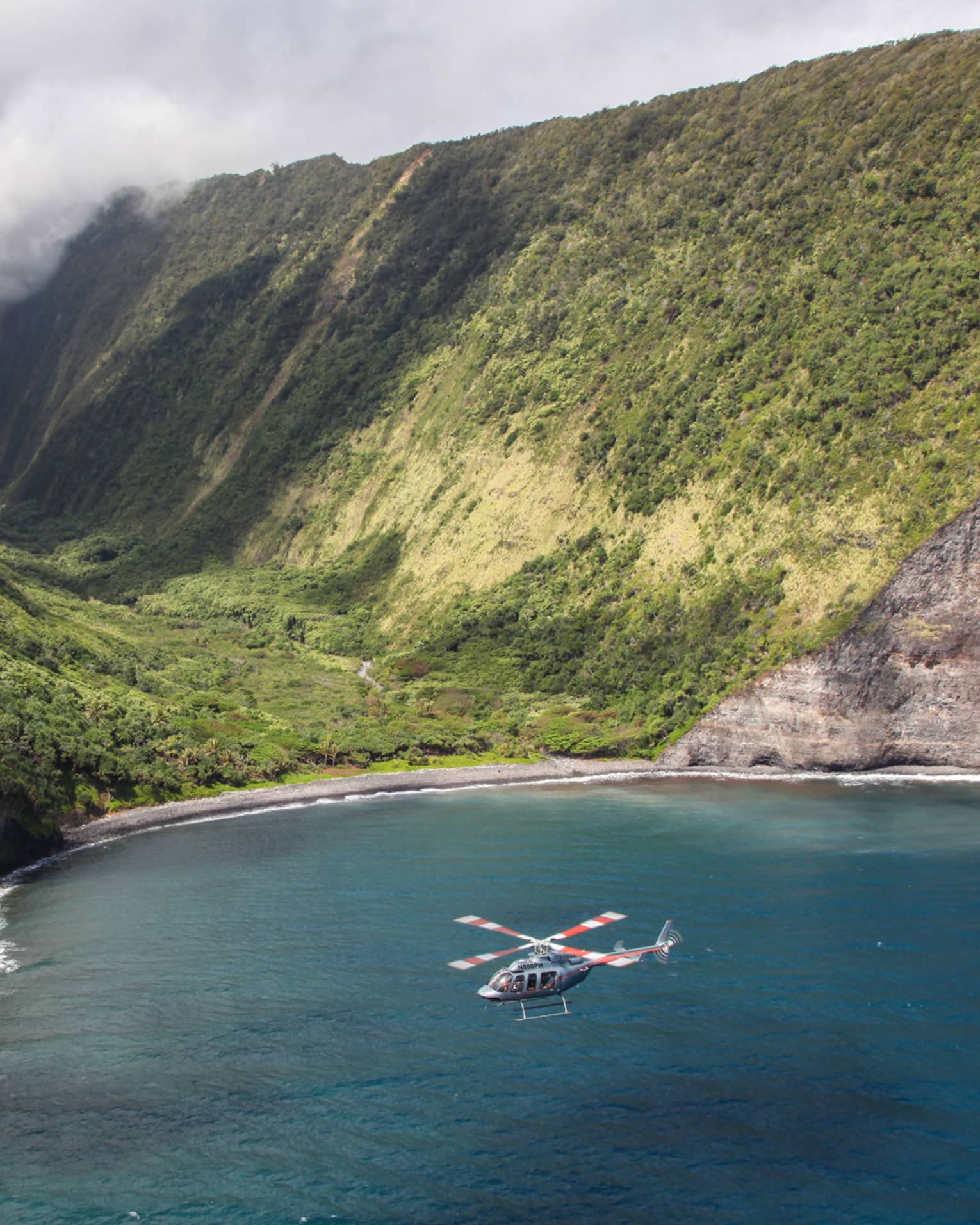 Helicopter flies over ocean by sweeping green volcanic mountains