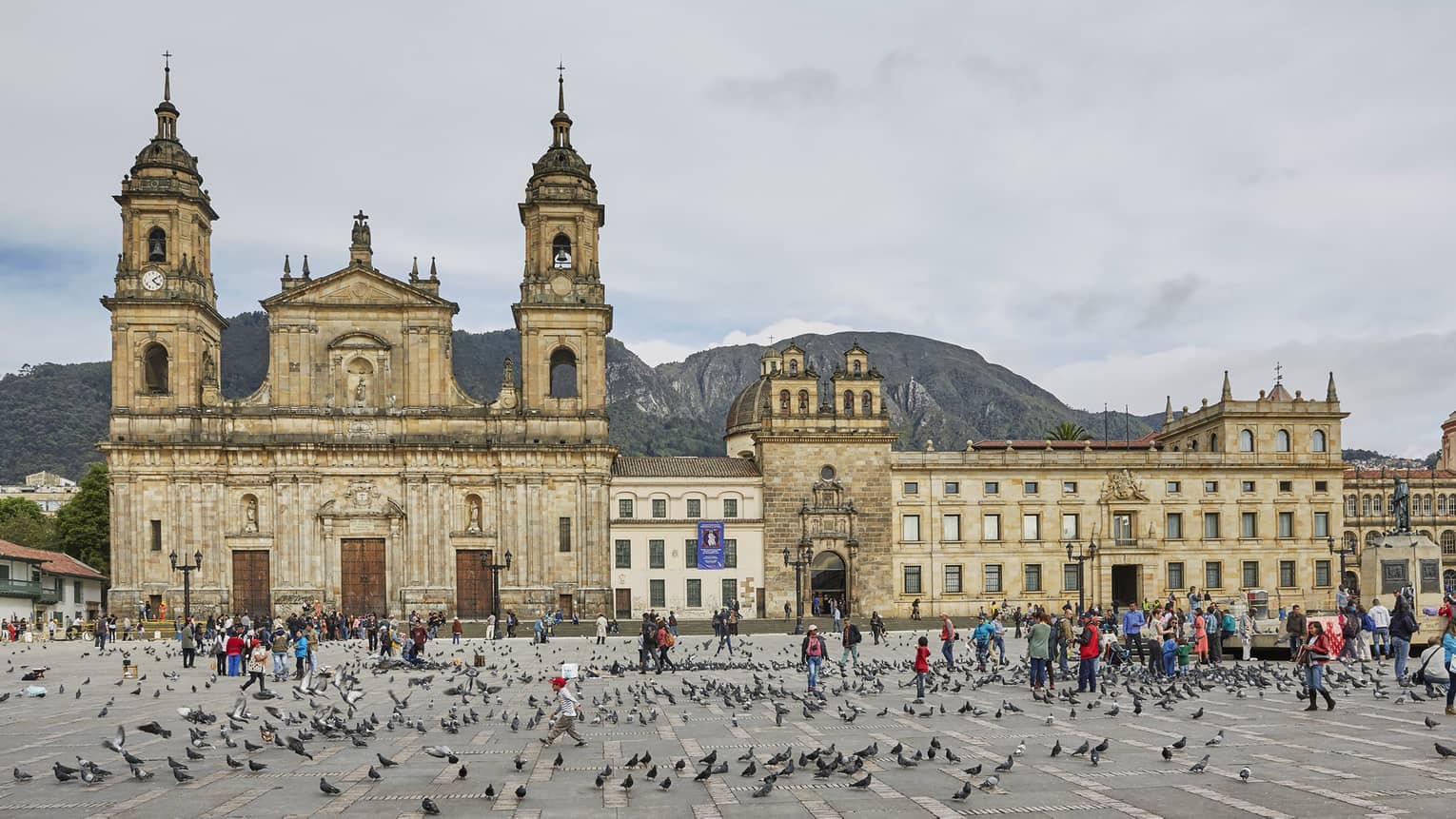 Pigeons and people crowd Bolivar Square in front of historic brick church, The Primatial Cathedral of Bogotá