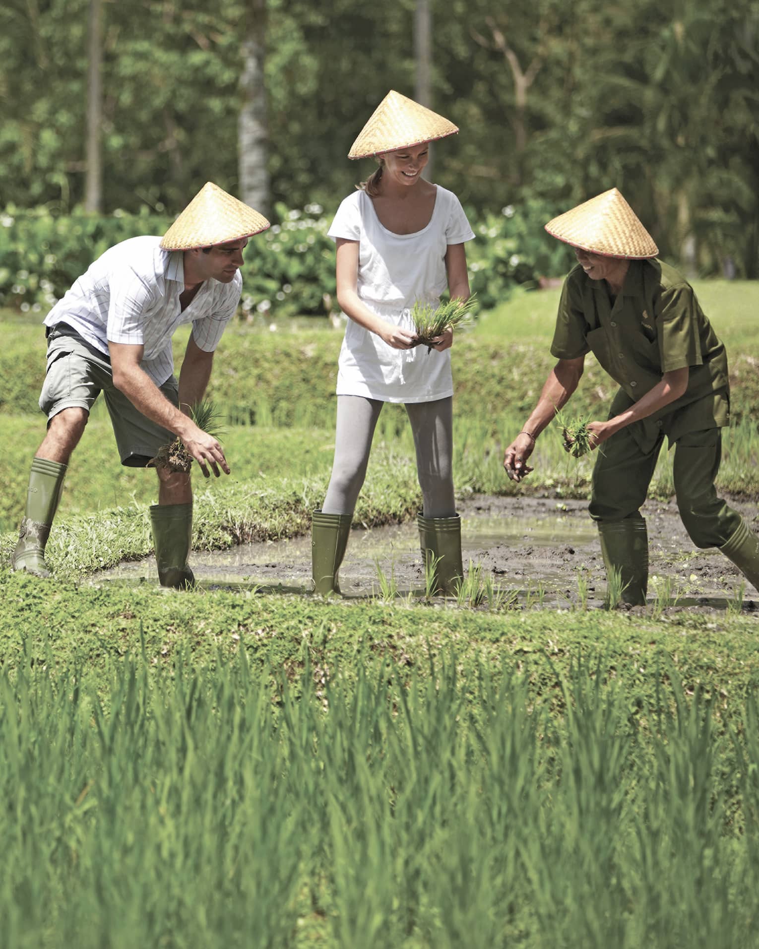 Man and woman in straw farmers hats kneel over garden, help gardener in rice paddie field