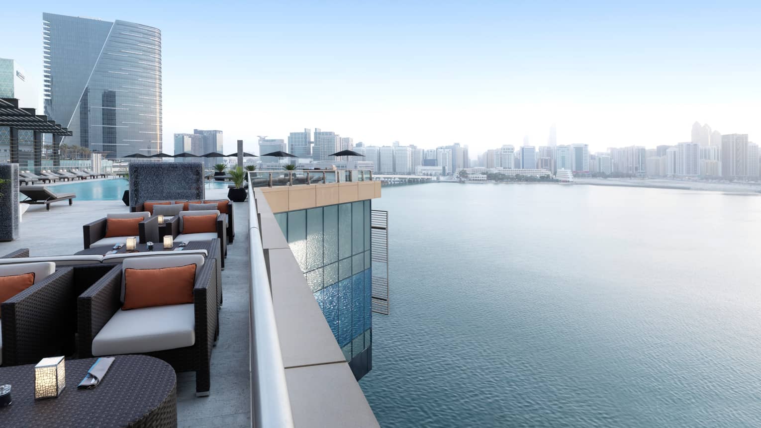 Rooftop lounge with stylish black wicker armchairs, cushions, candles on tables, swimming pool, overlooking Arabian Gulf