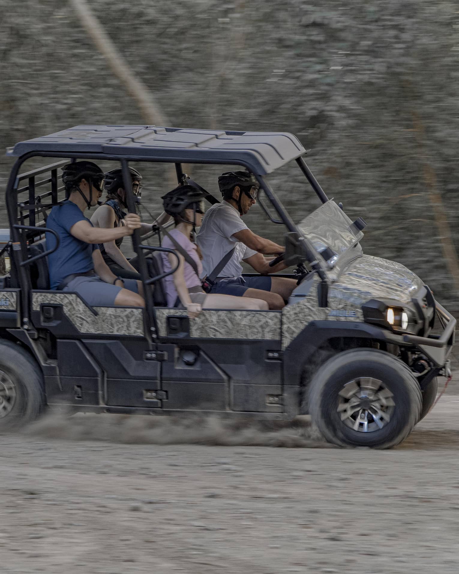 Four people speed along a dirt road in a 4x4 vehicle