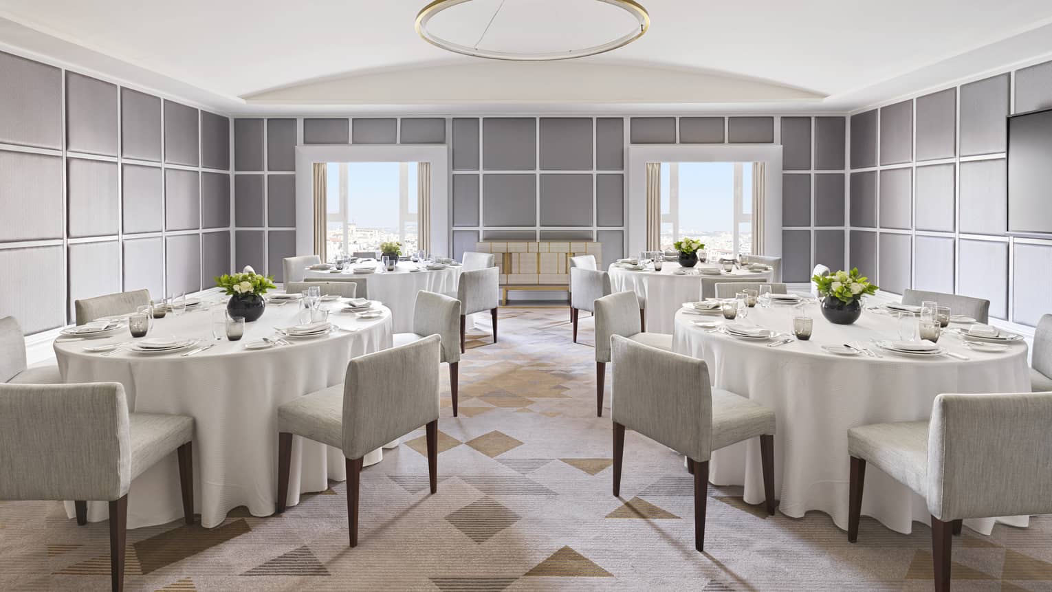 Several tables with white linens and square grey chairs.