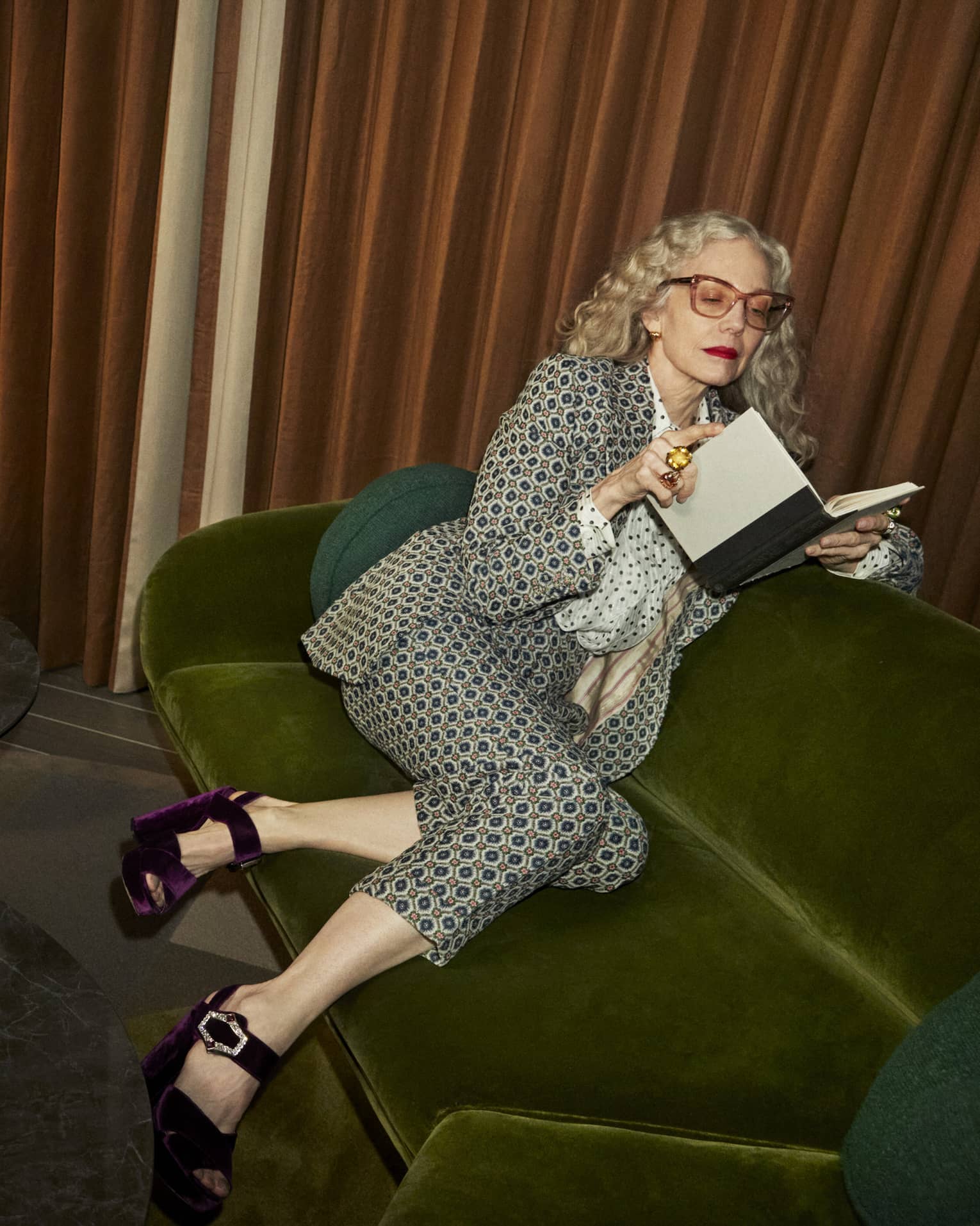 Woman sitting on green couch reading a book.