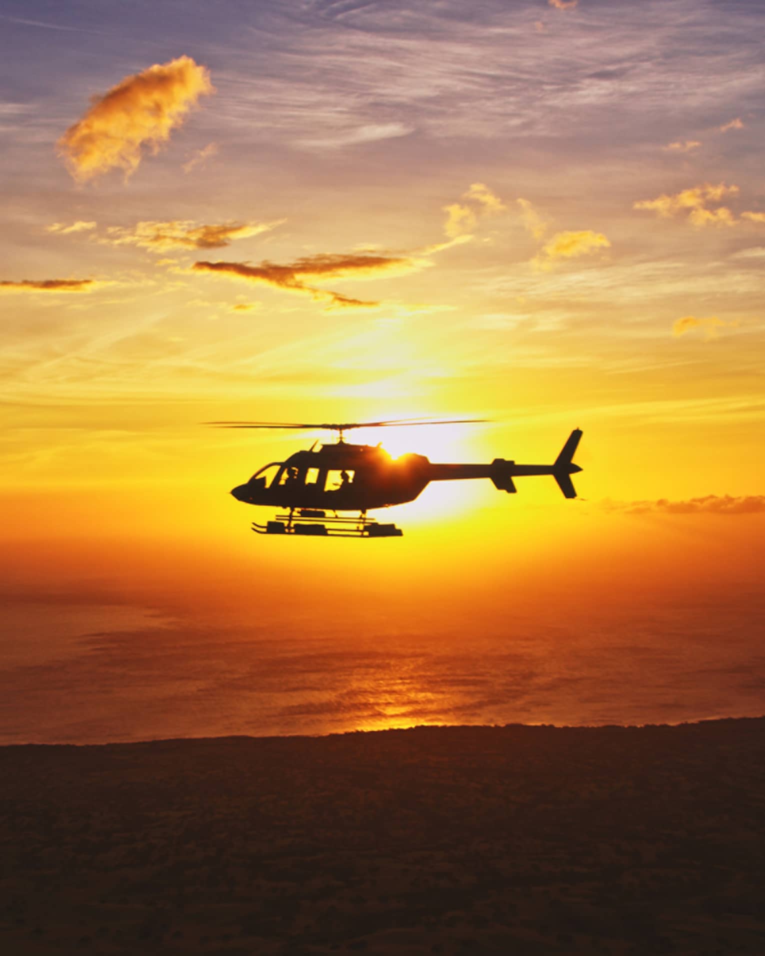 Silhouette of helicopter against orange sunset