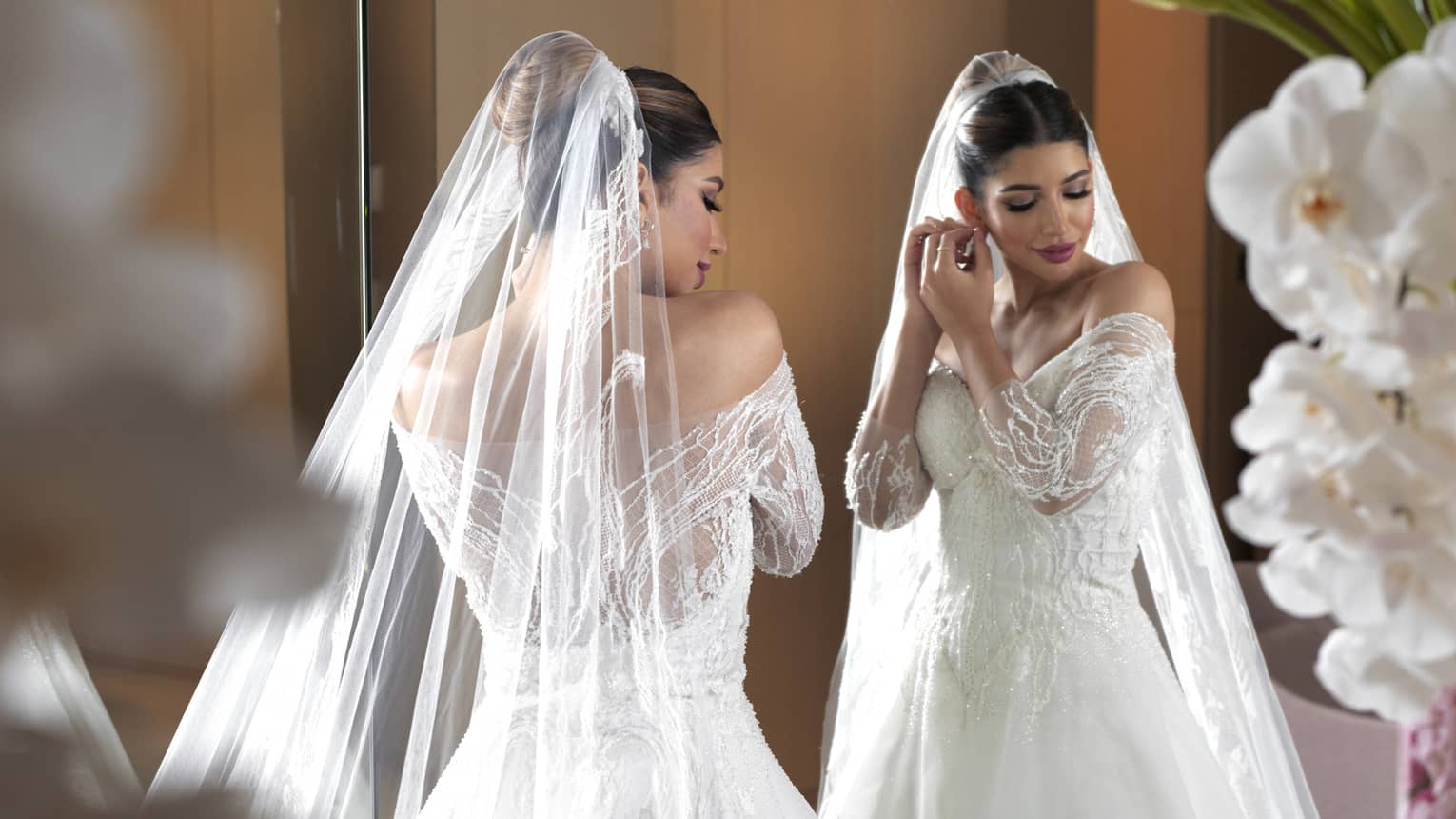 A bride in a white dress adjusting her earring in a mirror