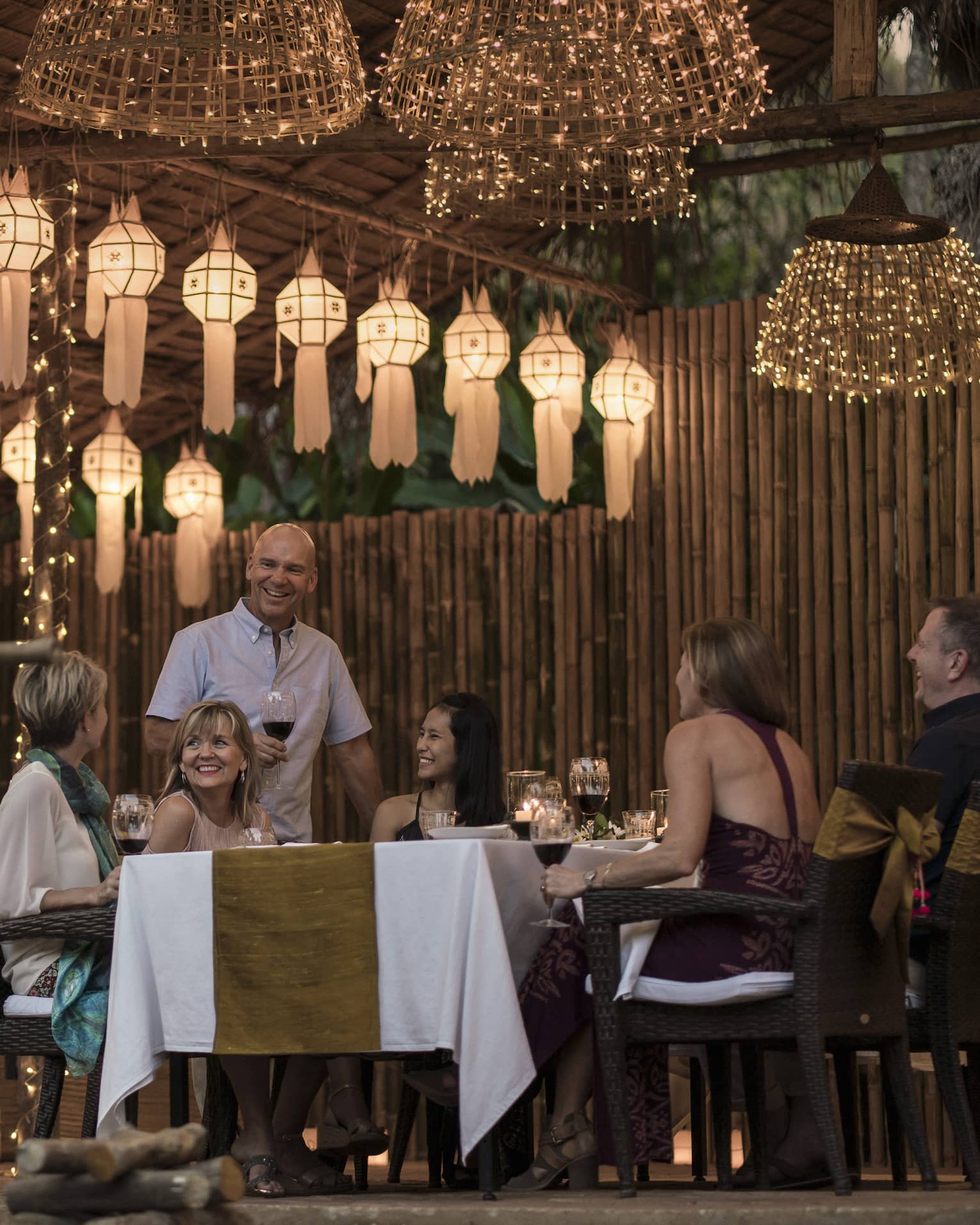 A group of people sitting at a table enjoying a meal in outdoor pavilion decorated with lanterns